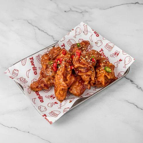 Korean Fried Chicken mit Spicy Yang Nyam Sauce, Sesam und roten und grünen Chiliringen auf Toriko-Papier.